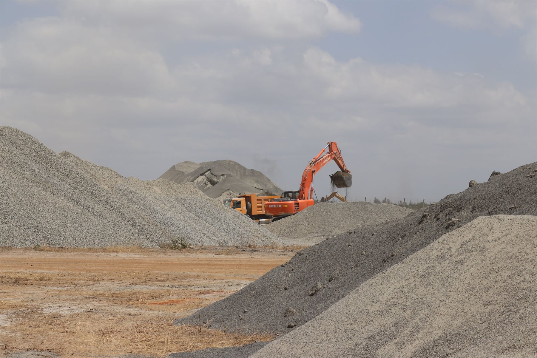 Aggregate stockpiles with an excavator in the background