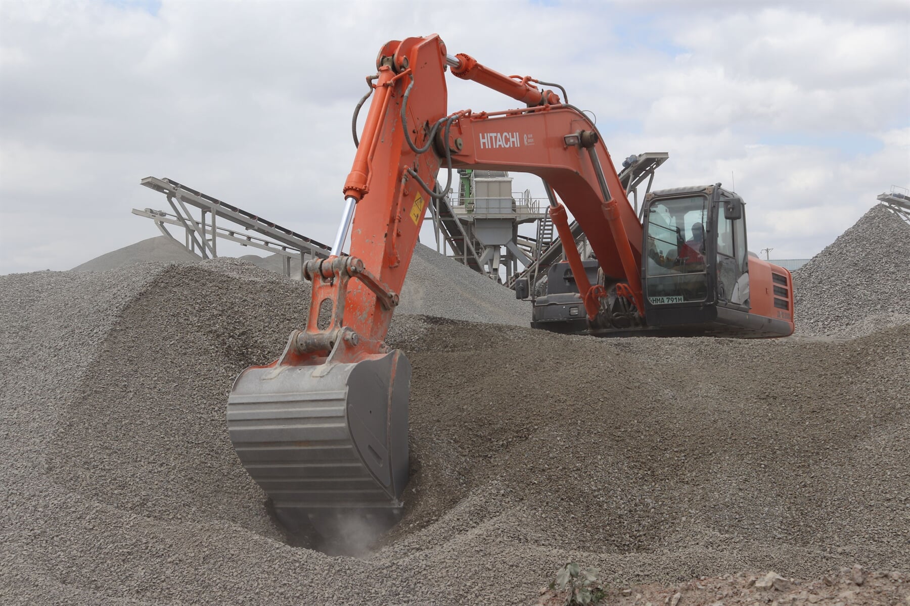 Excavator working beside aggregate stockpiles